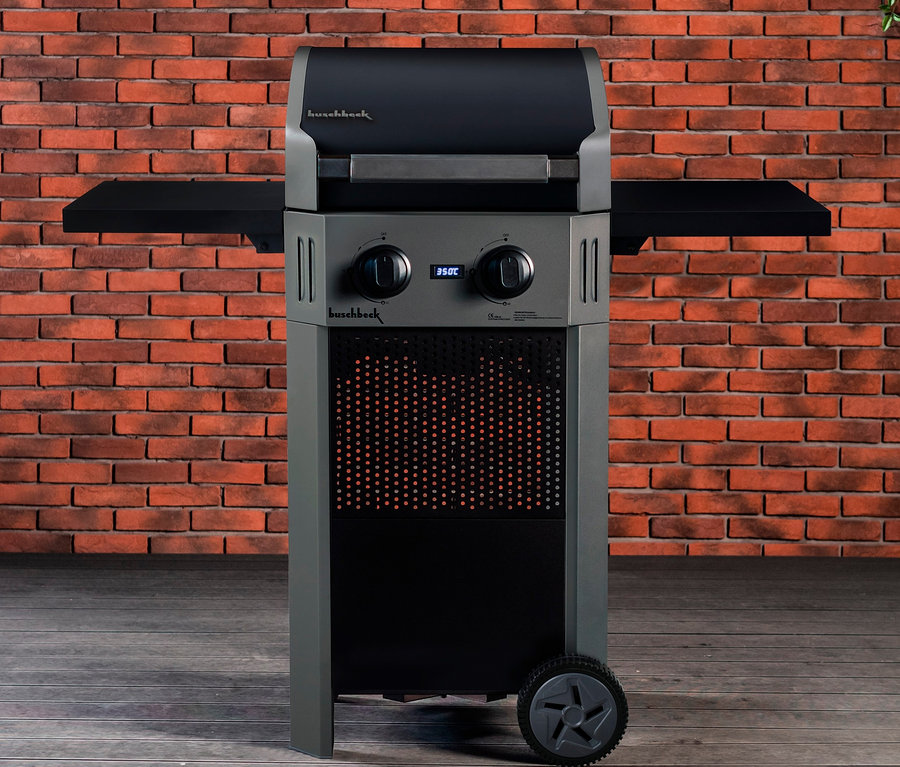 Ein grauer Buschbeck Elektrogrill »Grenada« mit 2 Brennern steht auf einem Holzboden vor einer Ziegelwand.