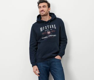 Mann posiert in marineblauem »Mustang« Hoodie und Jeans.