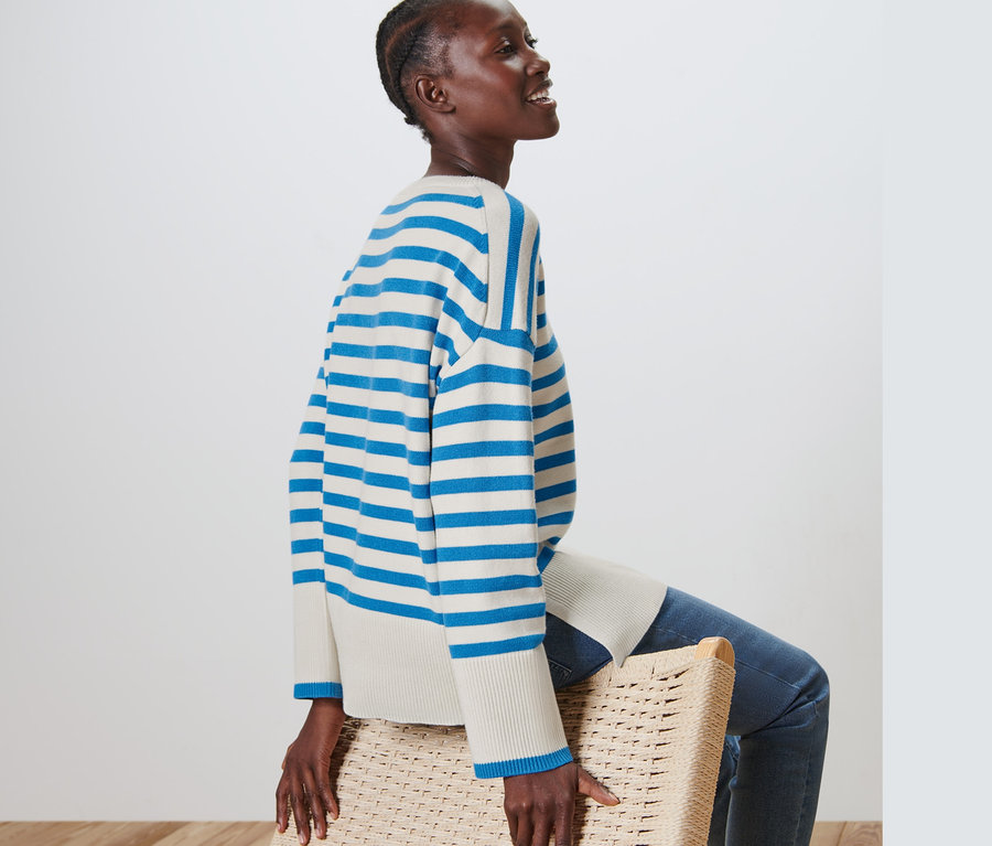 Frau sitzt auf einem Korbstuhl und trägt einen gestreiften Strickpullover.