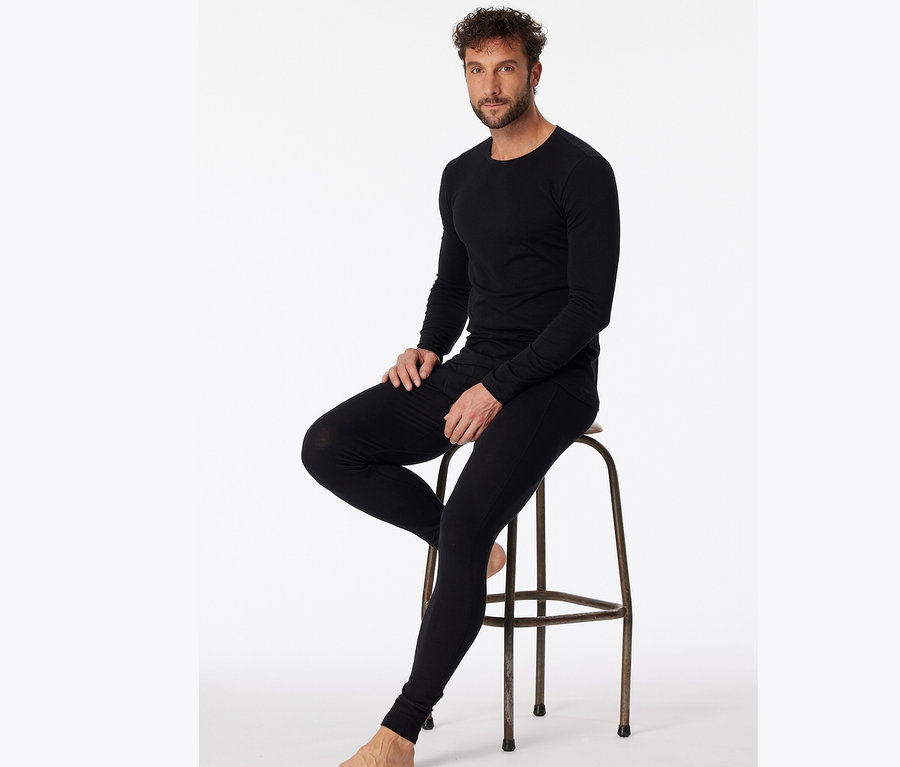 Mann sitzt auf einem Hocker und trägt ein schwarzes SCHIESSER Langarmshirt mit Bio-Baumwolle.
