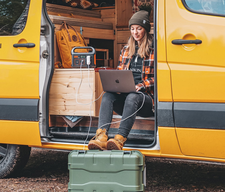 Frau sitzt in gelbem Van und benutzt Laptop, der von Jackery Explorer 240 und SolarSaga 100 betrieben wird.