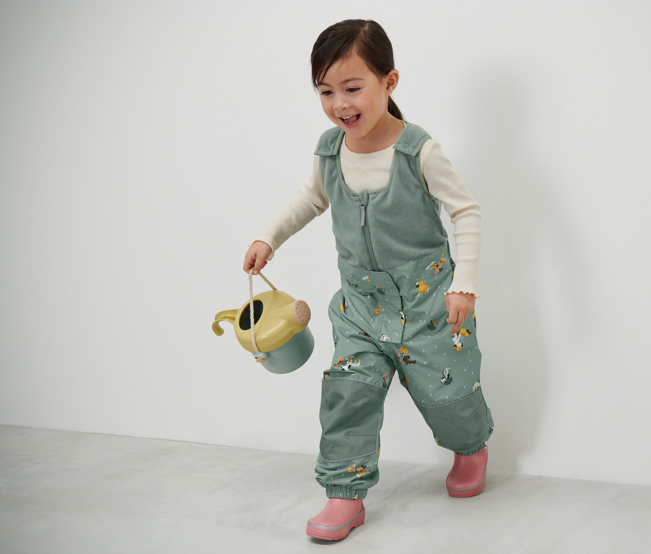Mädchen trägt eine Kinder-Thermo-Regenhose und hält eine Gießkanne.