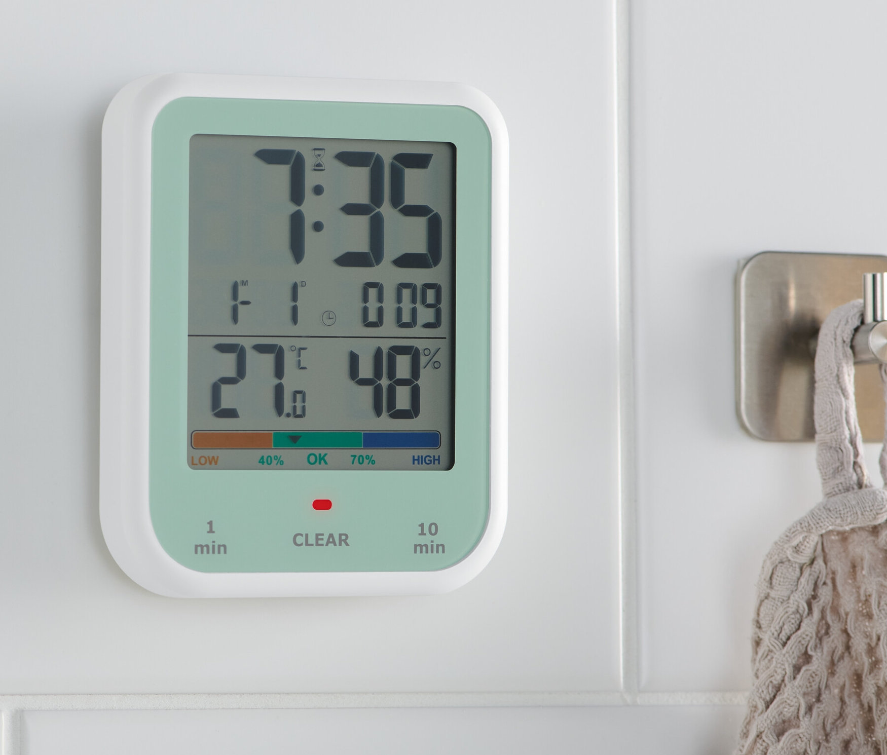 Eine digitale Uhr mit Hygro- und Thermometer hängt an einer weißen Wand. Das Display zeigt 7:35 Uhr, 27 Grad und 48% Luftfeuchtigkeit.