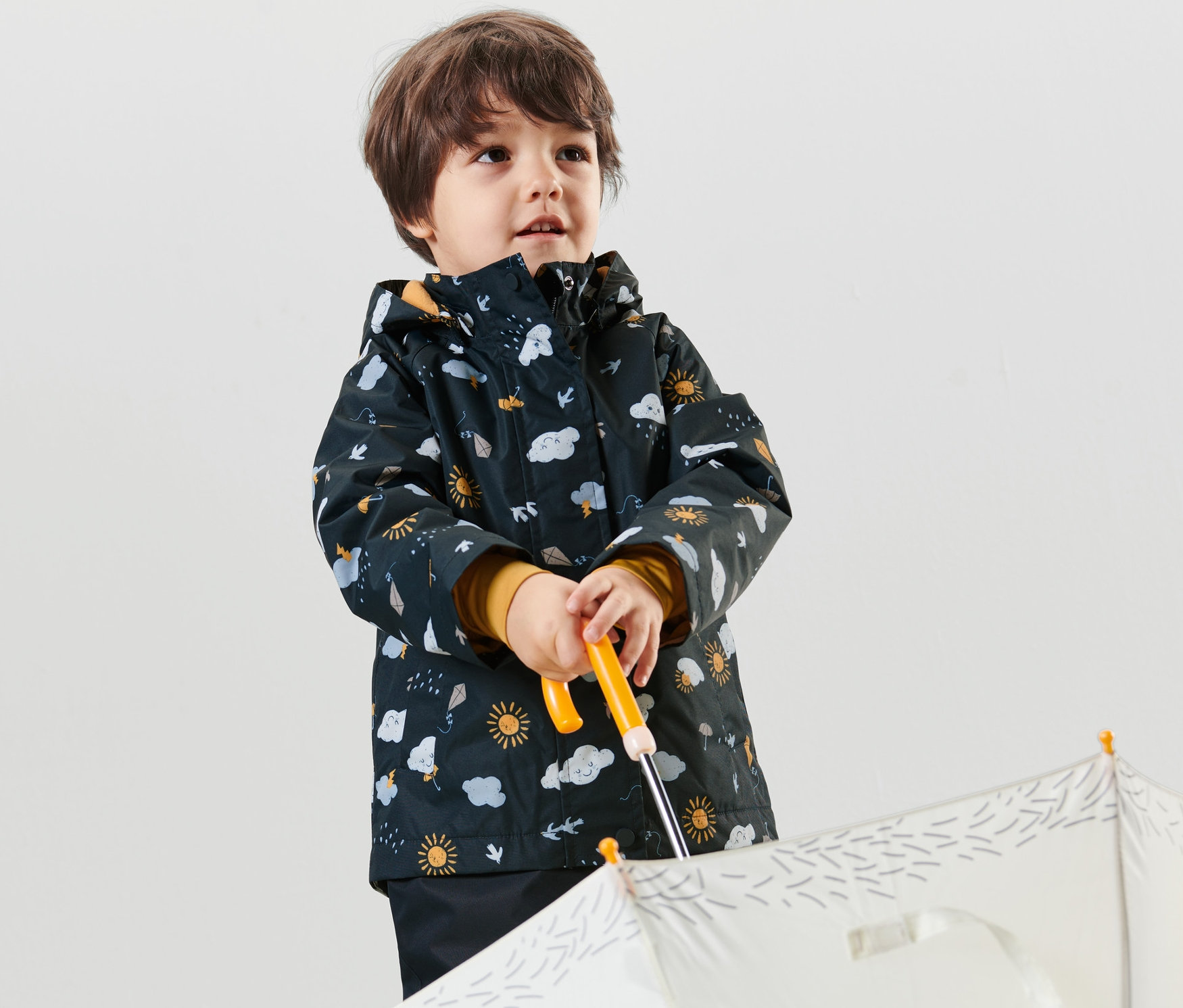 Junge hält einen weißen Regenschirm und trägt eine dunkelblaue Kleinkind-Thermo-Regenjacke mit Alloverprint.