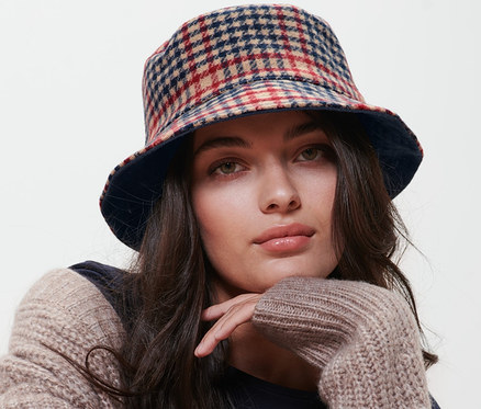 Frau sitzt auf einem Stuhl und trägt einen wendbaren Bucket Hat.