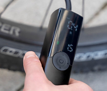 Hand hält elektrische Pumpe »VoltPump« am Fahrrad.