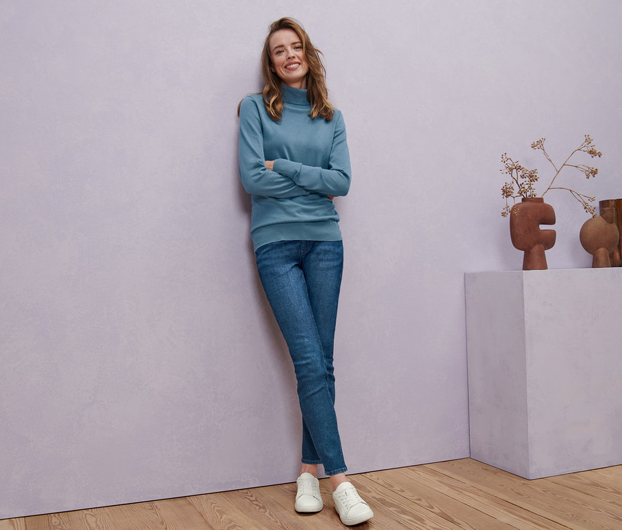 Frau posiert in rauchblauem Feinstrick-Rollkragenpullover, Skinny-Denim »Fit Hanna« und Ledersneakern.