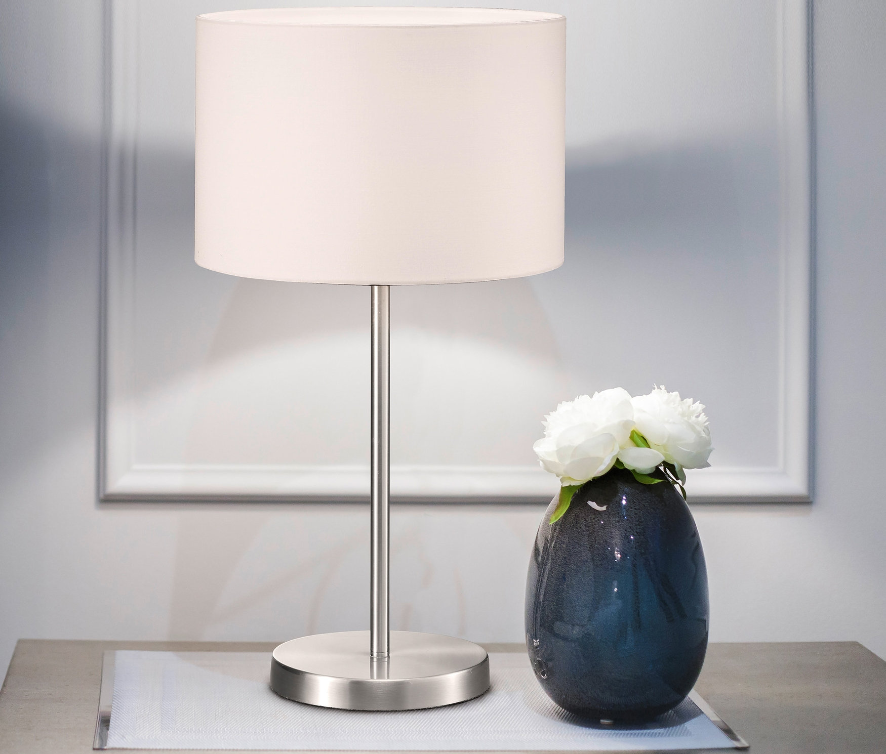 Nachttisch mit Trio Tischleuchte »Hotel« und Vase mit weißen Blumen.