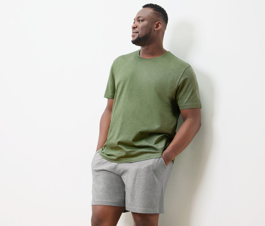 Mann im Shorty-Pyjama steht an einer Wand.