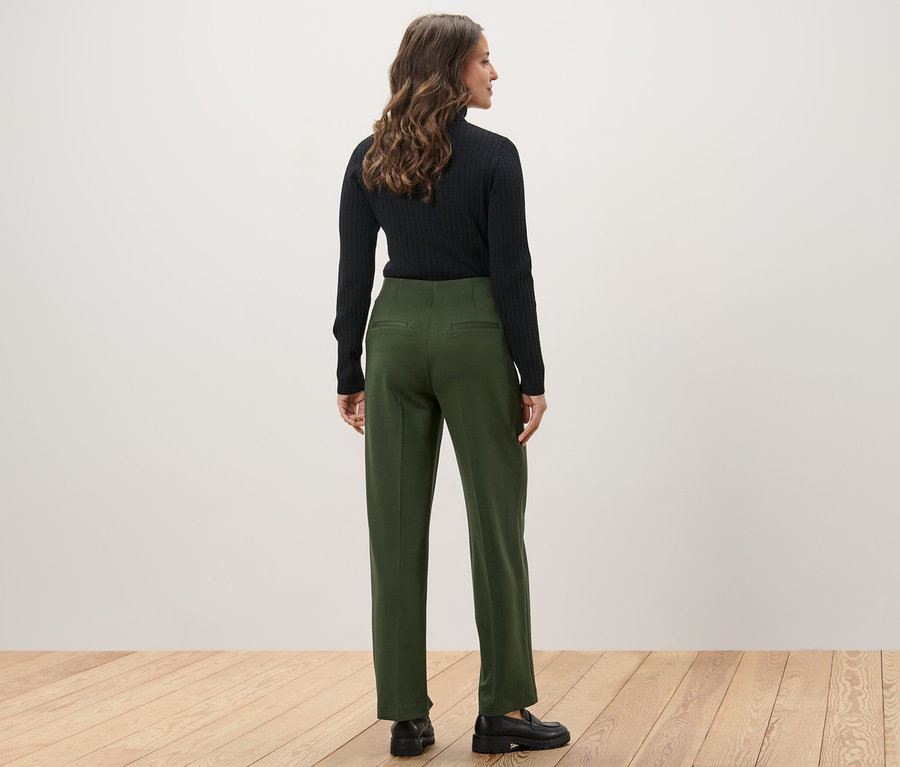 Eine Frau steht mit dem Rücken zur Kamera und trägt ein schwarzes Oberteil und eine grüne Jerseyhose.