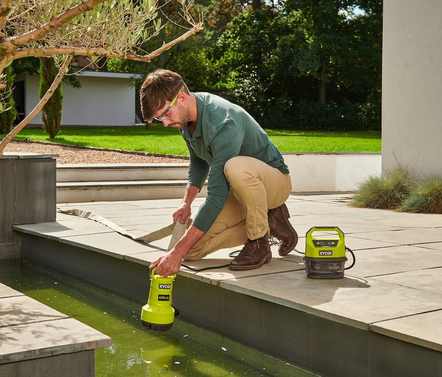 Mann setzt RYOBI 18 V One+ Akku-Tauchpumpe in einen Gartenteich.