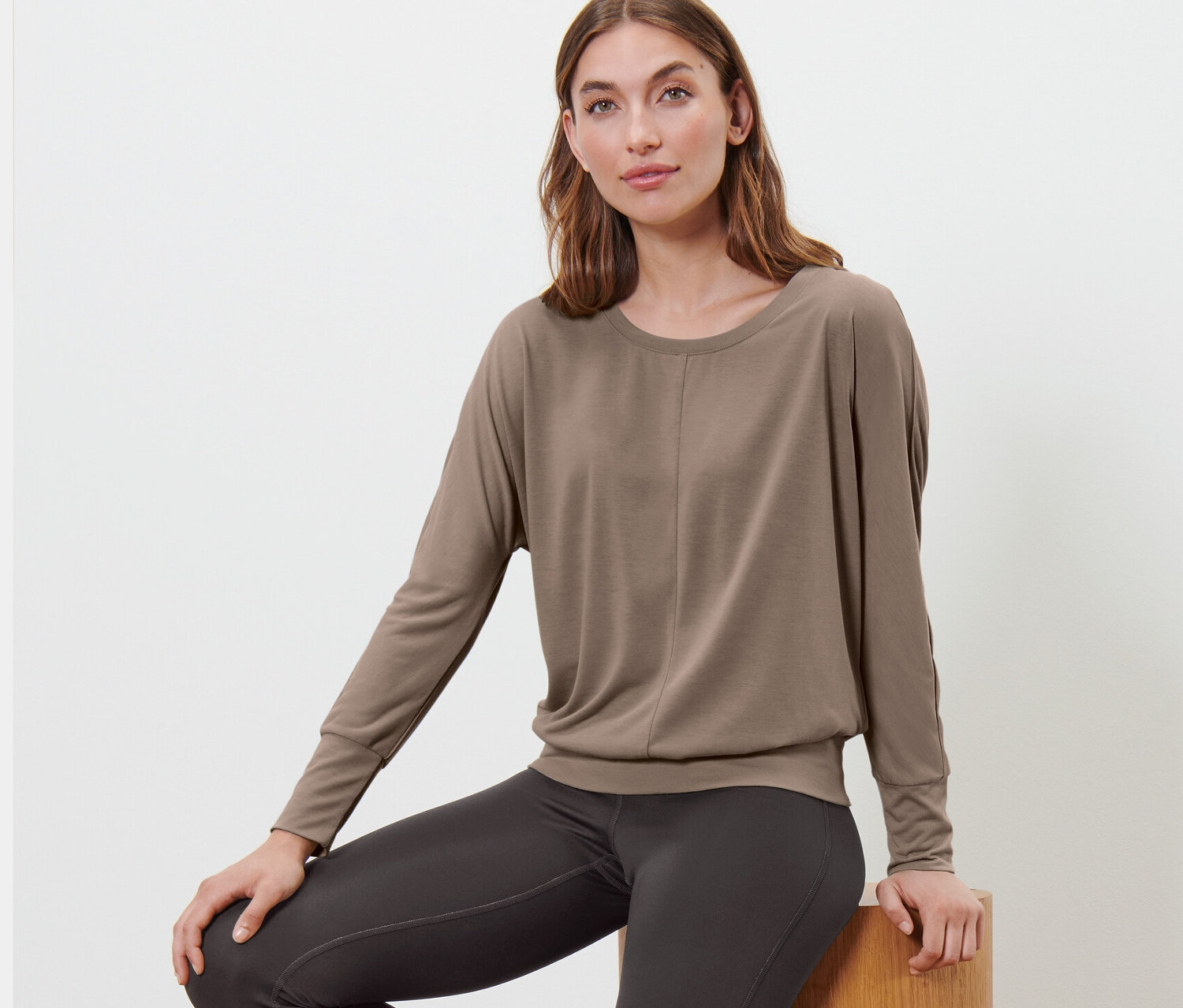 Frau sitzt auf Holzstufen und trägt ein taupefarbenes Sport-und-Yogashirt.