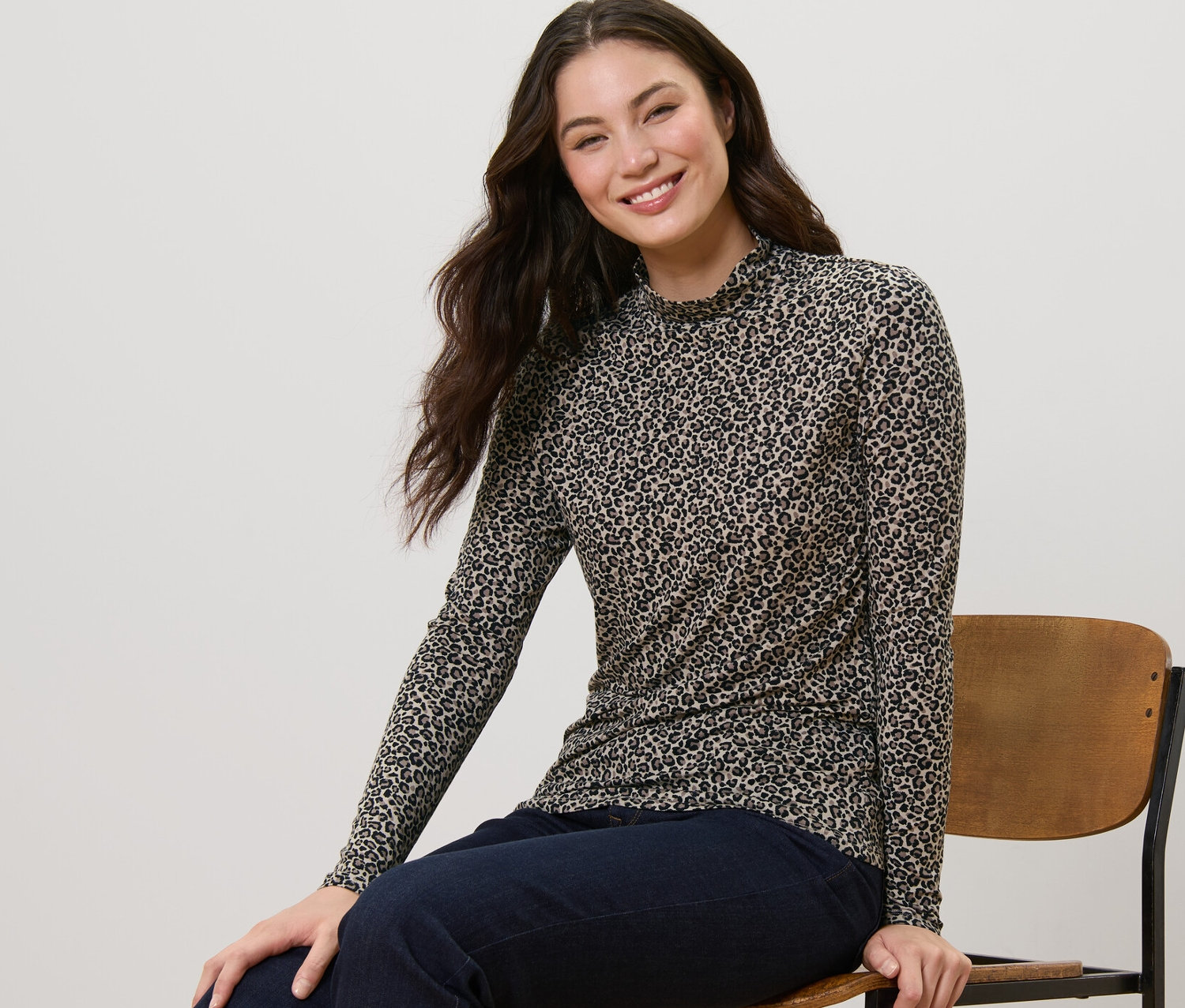 Eine Frau sitzt auf einem Stuhl und trägt ein bedrucktes Blusenshirt mit Stehkragen.