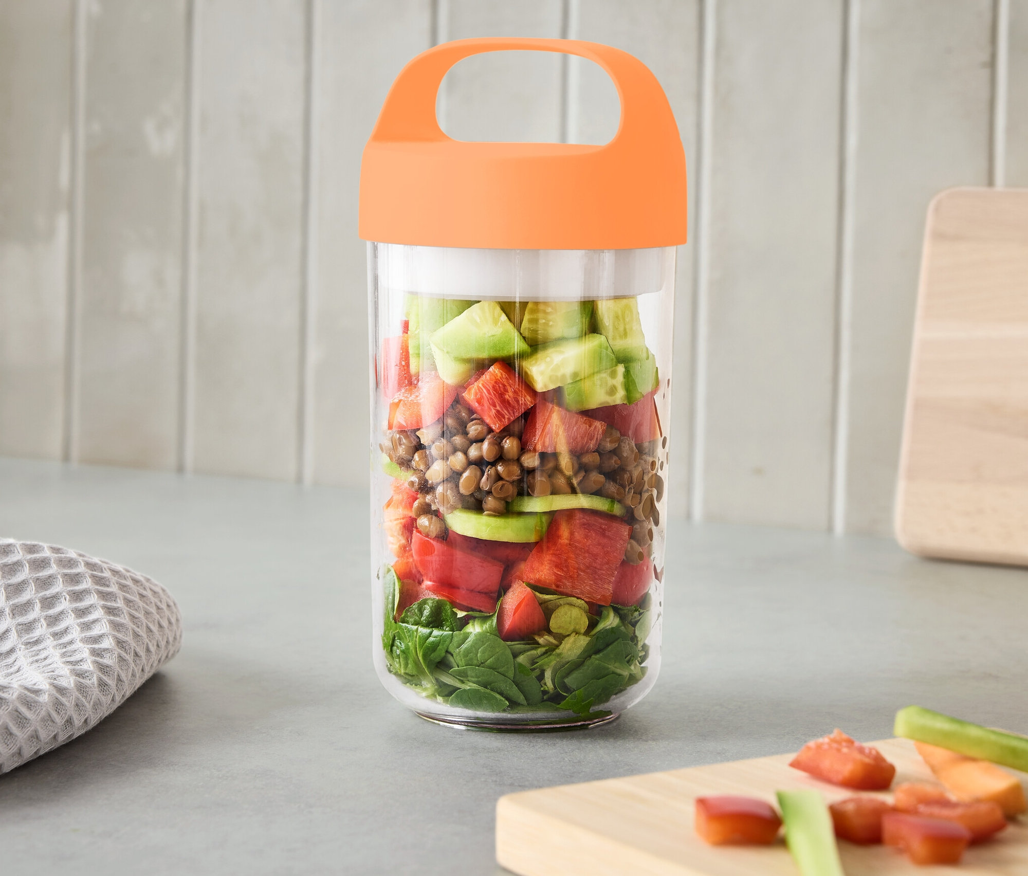 Ein großer To-Go-Behälter mit Henkel, gefüllt mit Gemüse, steht auf einer Küchentheke.