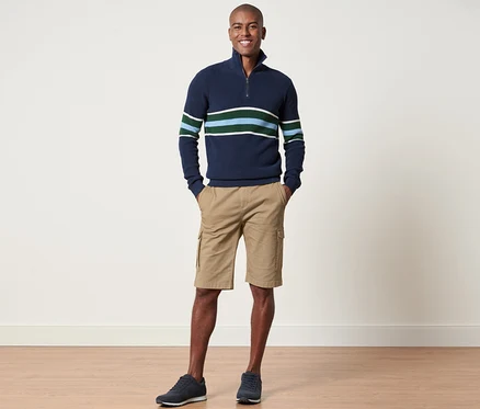 Mann steht und posiert in einem marineblauen Streifenpullover und sandfarbenen Cargo-Shorts.