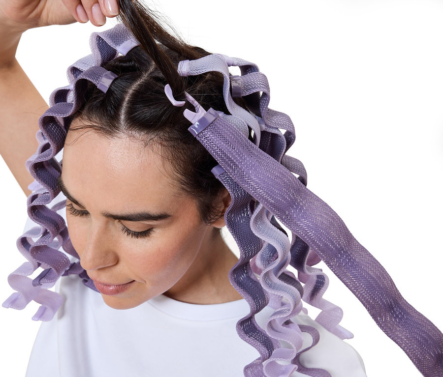 Frau wickelt Haare mit lila Lockenwicklern ein.