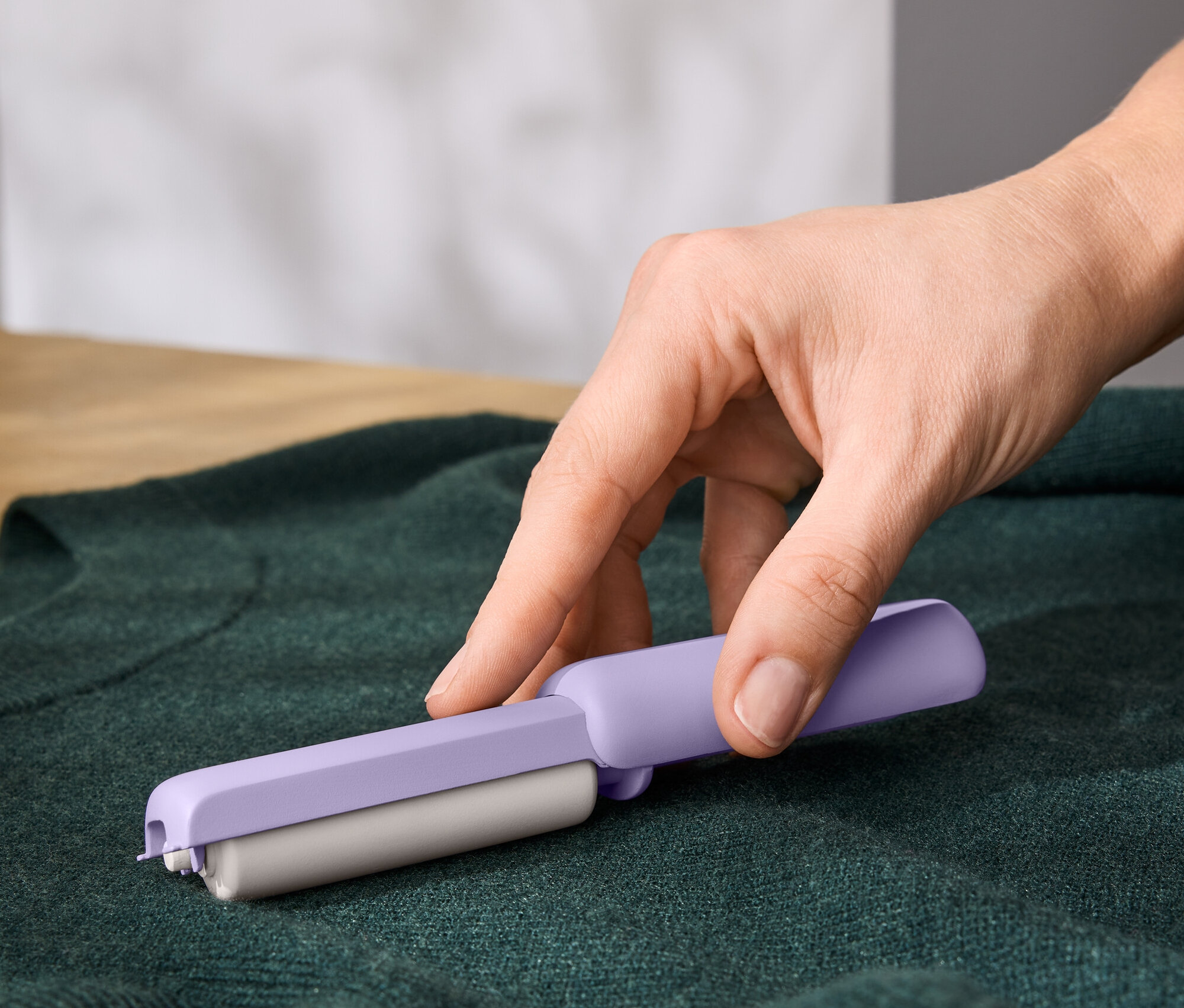 Hand benutzt einen lila Fusselentferner auf einem grünen Pullover.