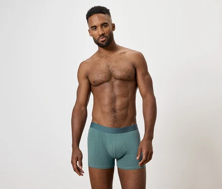 Mann mit freiem Oberkörper posiert in grünen Boxershorts.