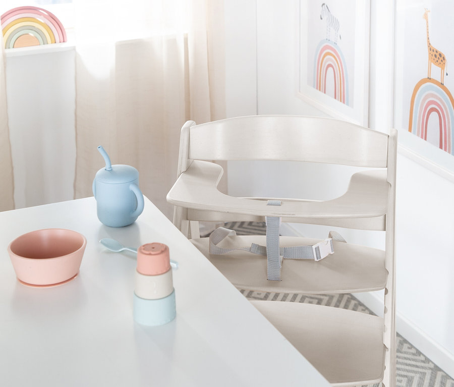 Auf einem weißen Tisch stehen eine rosa Schüssel, ein blauer Becher mit Strohhalm und ein Stapelspielzeug neben einem roba Babyhochstuhl »Sit Up Flex«.