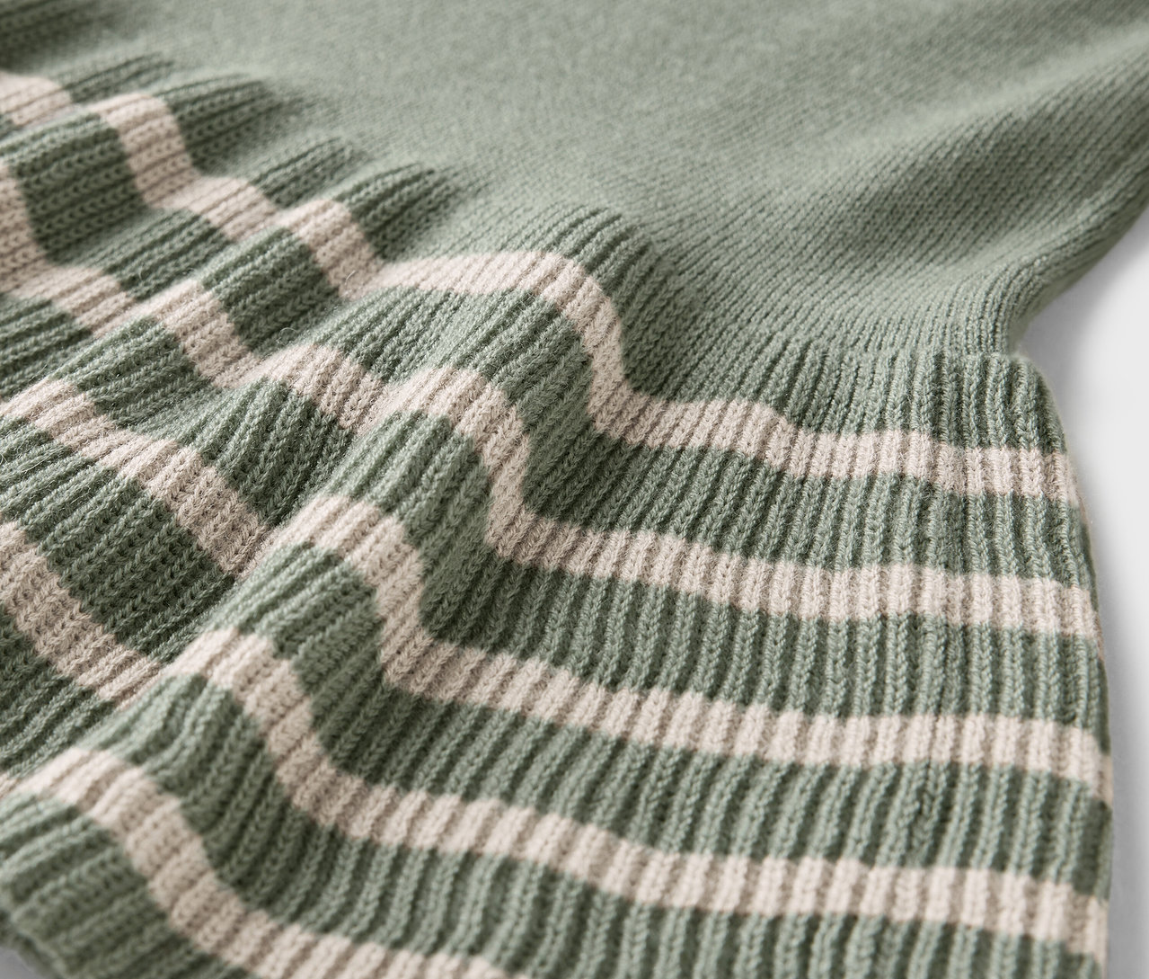 Detailansicht eines grünen Pullovers mit cremefarbenen Streifen.