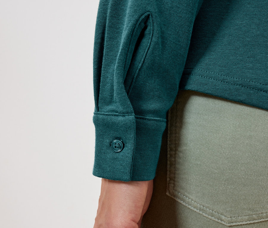 Detail eines grünen Langarmshirts mit Knopf an der Manschette und olivgrünen Jeans.