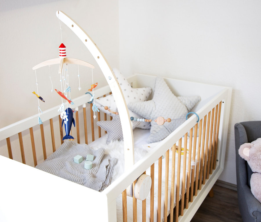Babybett mit weißem Rahmen, Holzstäben und Sternkissen. Darüber hängt ein small foot Mobile mit Halterung »Seaside« mit maritimen Motiven.