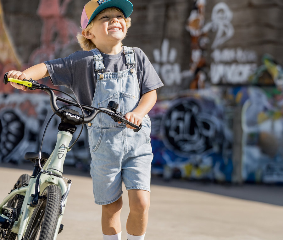 Ein Junge steht neben seinem mintgrünen PUKY LS-PRO 16 Fahrrad und lächelt.
