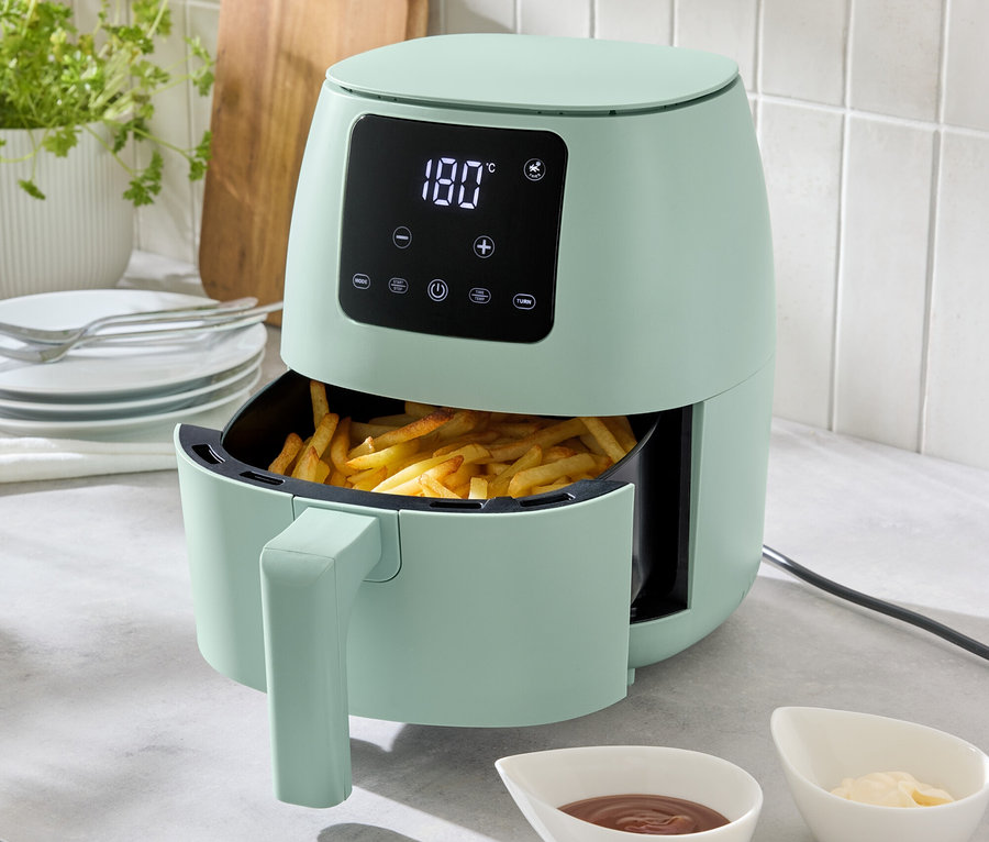 Eine hellgrüne Heißluft-Fritteuse, 2 l, steht auf einer Küchentheke, gefüllt mit Pommes Frites. Zwei Schälchen mit Soßen stehen davor.
