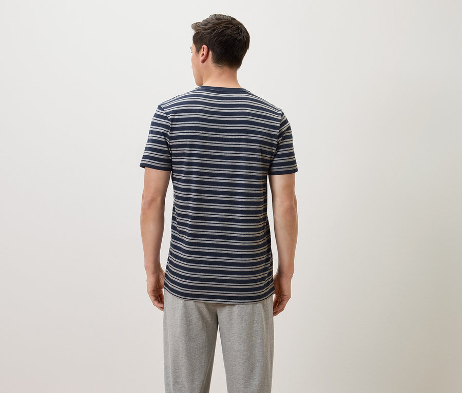 Ein Mann von hinten, der ein blau-grau gestreiftes T-Shirt und graue Jogginghose trägt.