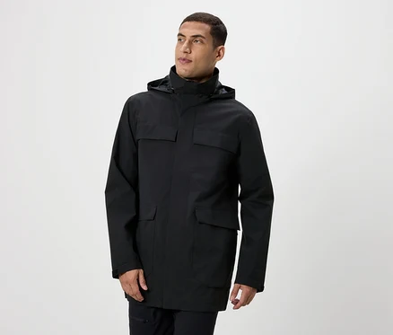 Mann posiert in einer schwarzen Jacke mit Kapuze und Taschen.