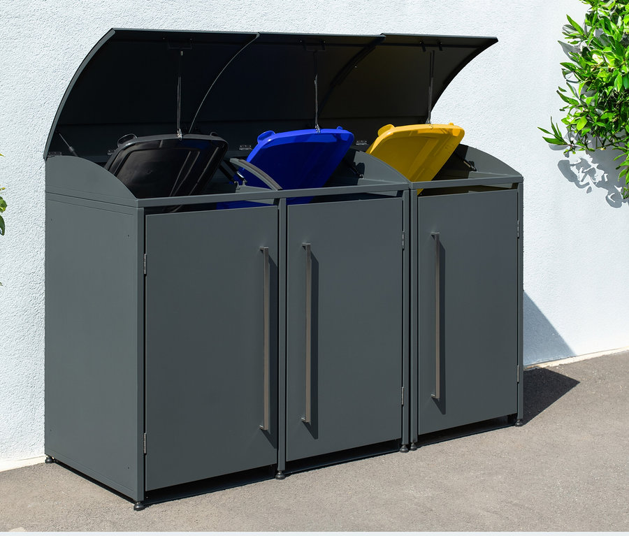 Graue Mülltonnenbox, 3er, steht draußen neben einem Busch.