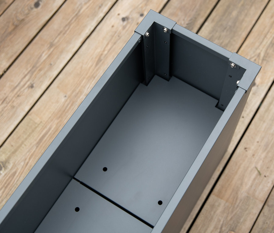 Draufsicht auf einen leeren, rechteckigen, grauen Pflanzkasten mit Einlegeboden auf einem Holzdeck.