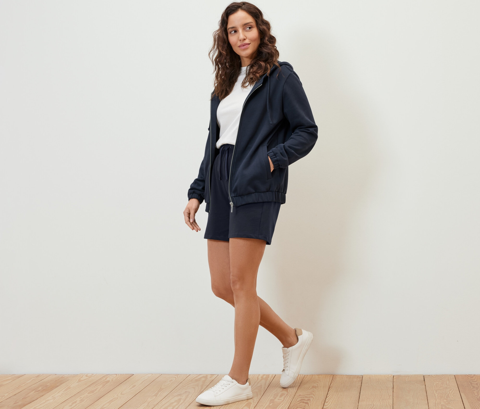 Frau geht, trägt eine dunkelblaue Sweatjacke und Shorts.