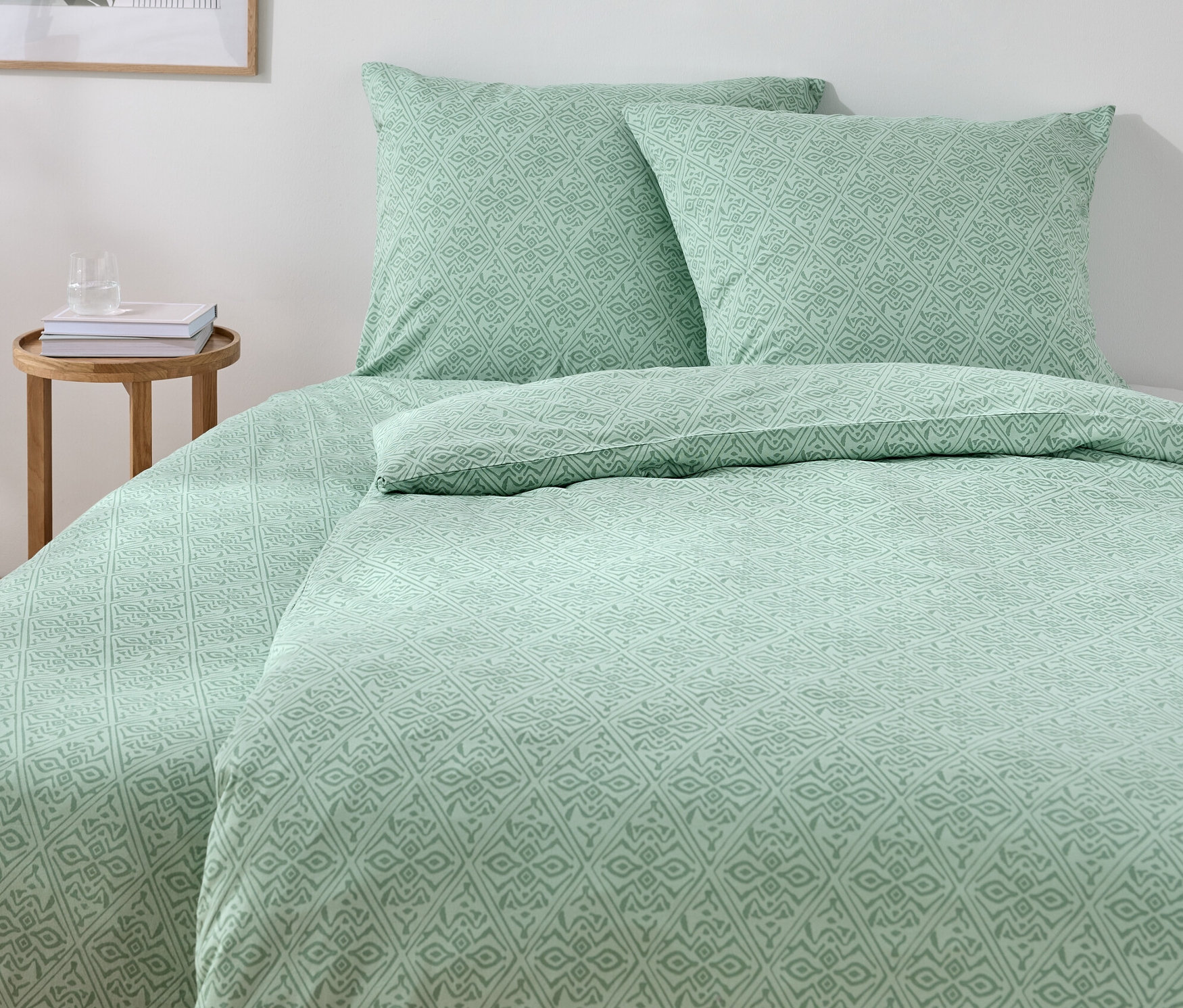 Grüne Jersey-Bettwäsche in Normal- und Übergröße auf einem Bett mit zwei Kissen und einem Holztisch.