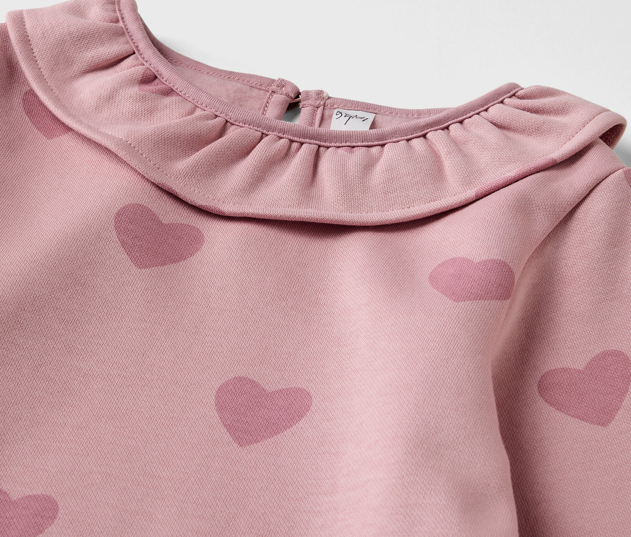 Detailansicht eines Kinder-Sweatkleids mit Rüschenkragen und Herzprint.