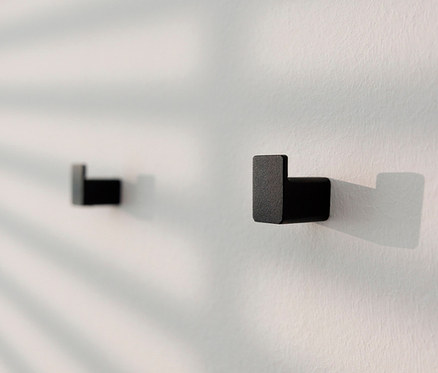 Zwei schwarze Wandhaken »Palo« an einer weißen Wand mit Blätterschatten.