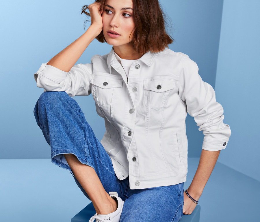 Eine Frau sitzt auf einem blauen Würfel und trägt eine Jeansjacke.