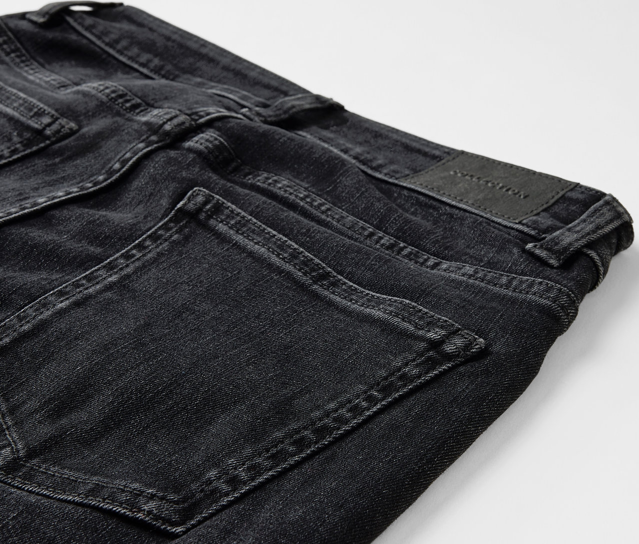 Detailaufnahme einer schwarzen Jeans mit Taschen und einem Lederpatch auf der Rückseite.