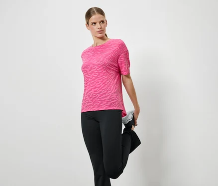 Frau dehnt Bein in einem pinken Sport-T-Shirt und schwarzen Hosen.