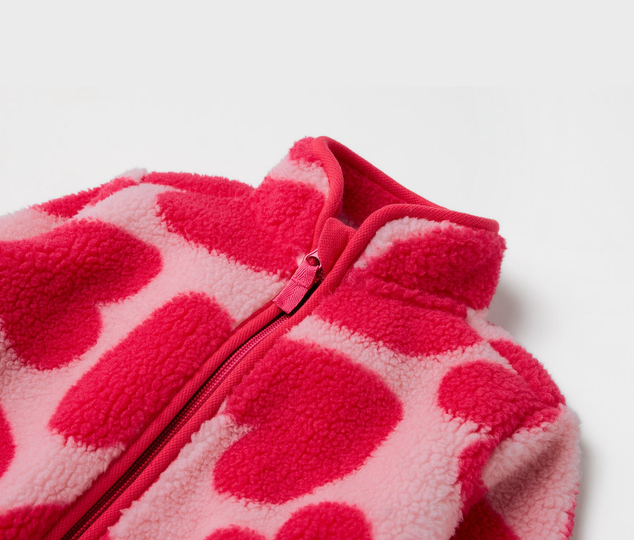 Detail einer rosa Fleecejacke mit Reißverschluss und Herzmuster.