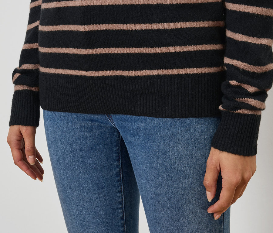Nahaufnahme einer Frau, die einen schwarz-braun gestreiften Pullover und blaue Jeans trägt.