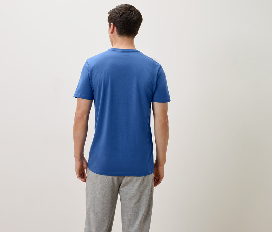 Rückansicht eines Mannes in einem blauen T-Shirt und grauer Jogginghose vor einem neutralen Hintergrund.