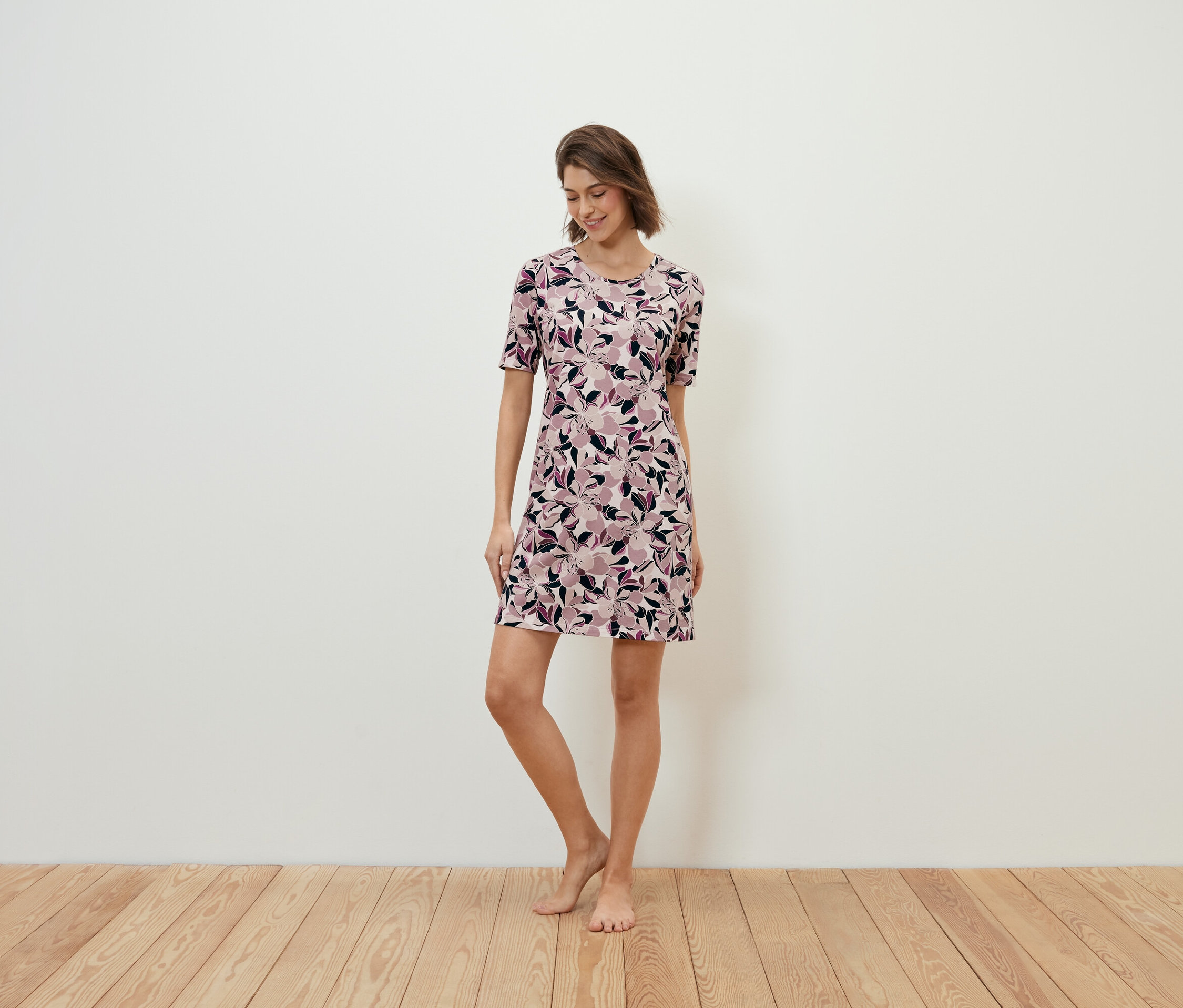 Frau steht auf Holzboden und trägt ein geblümtes Kleid.