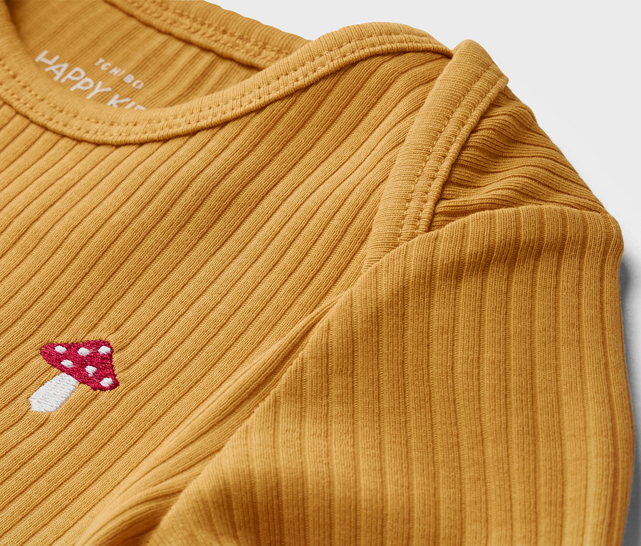 Detailansicht eines gelben Baby-Langarmshirts mit Rippstruktur und einer Fliegenpilzstickerei.