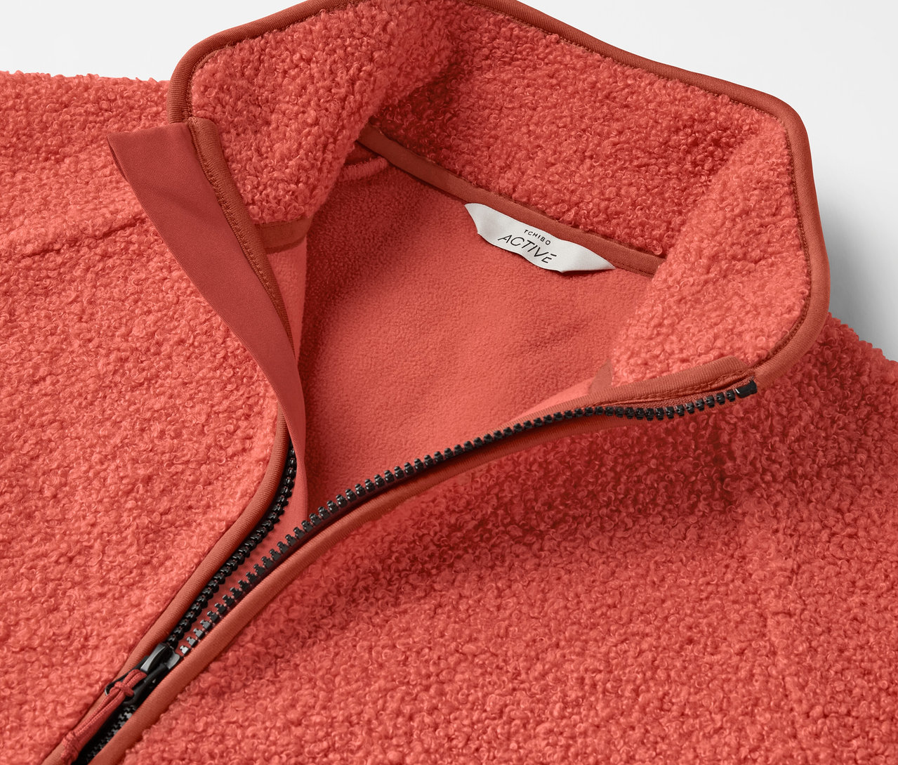 Detailansicht einer korallenroten Fleecejacke mit Reißverschluss.