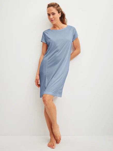 Frau lehnt an einer Wand und trägt ein blaues Kleid.