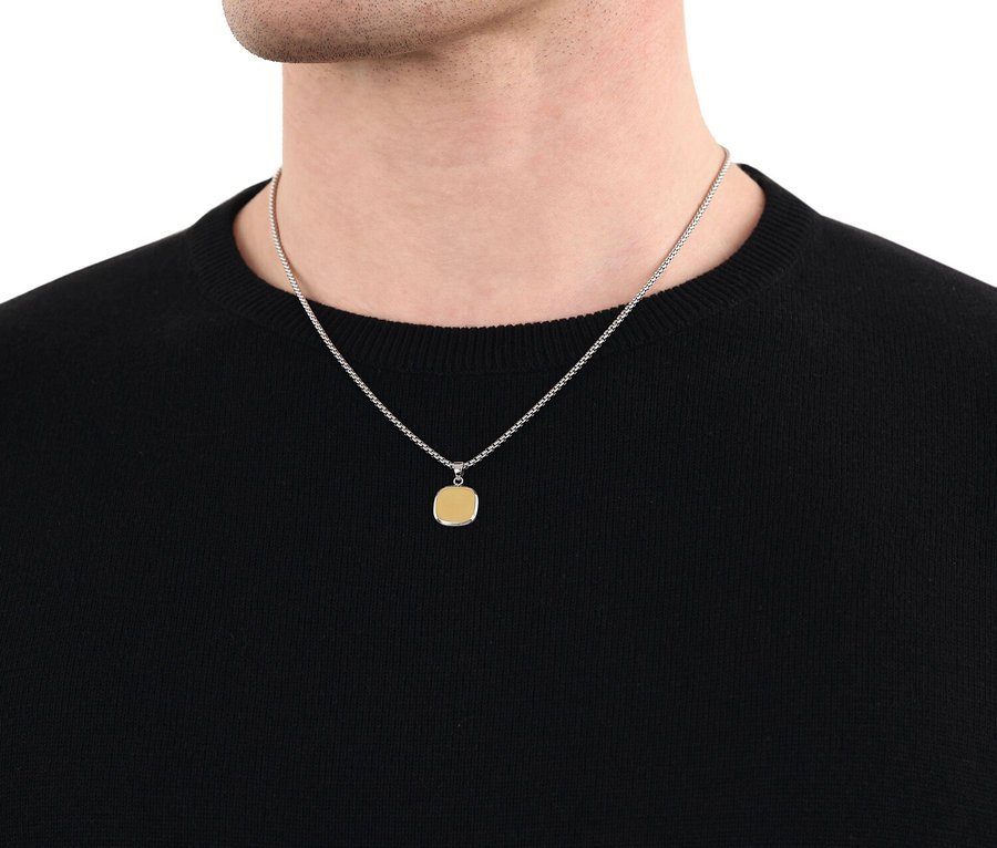 Nahaufnahme eines Mannes mit einer silbernen Halskette mit einem quadratischen, goldenen Anhänger, der über einem schwarzen Pullover hängt.