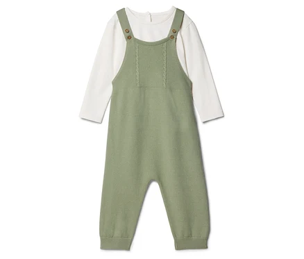 Ein grüner Baby-Strampler aus Strickstoff liegt über einem weißen Langarmshirt.
