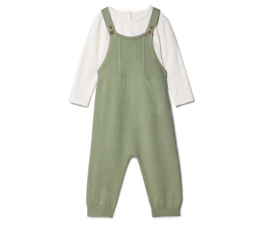 Ein grüner Baby-Strampler aus Strickstoff liegt über einem weißen Langarmshirt.