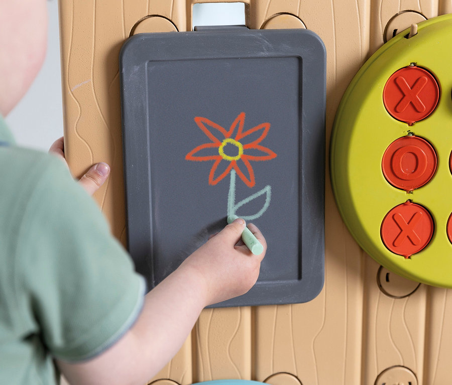 Kind zeichnet mit Kreide eine Blume auf die graue Tafel der Smoby Life Activity Wall.